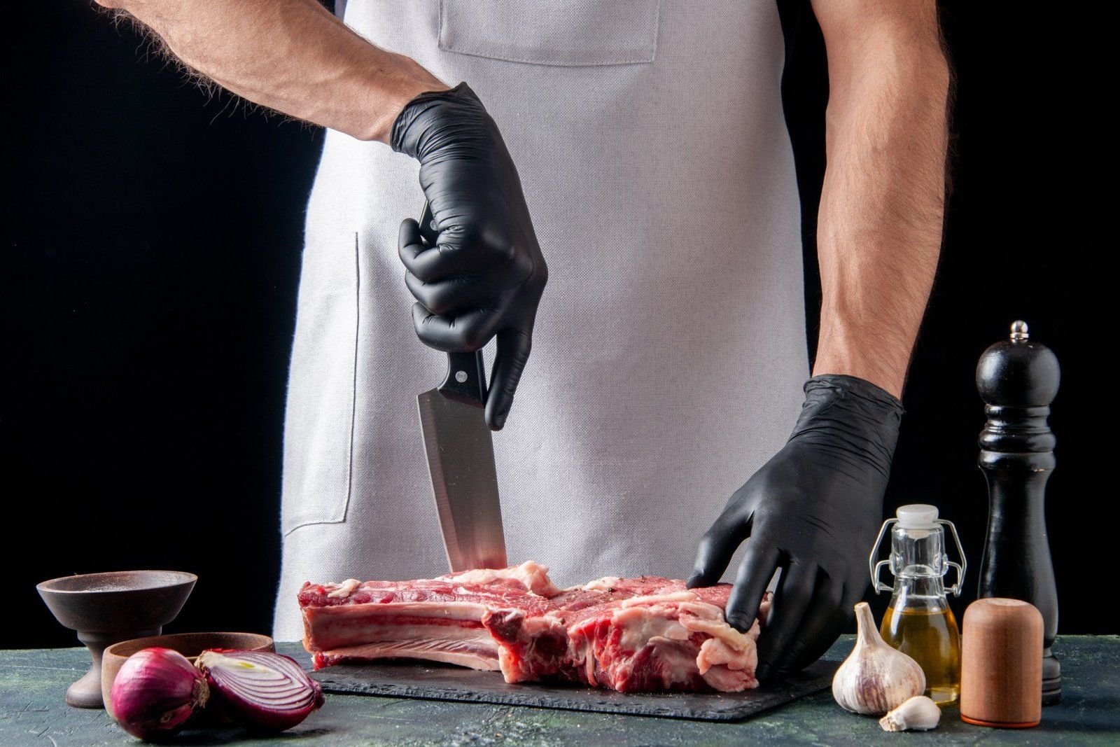 A professional butcher wearing black gloves portions a thick piece of raw bone-in beef.