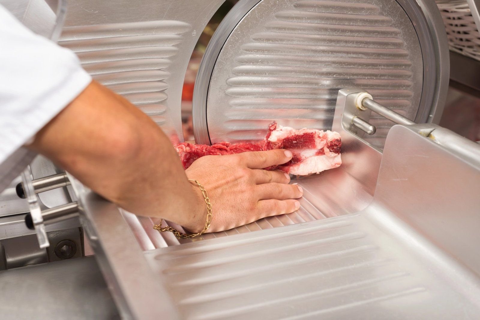 A butcher guides raw beef through a commercial meat slicer for uniform cuts.