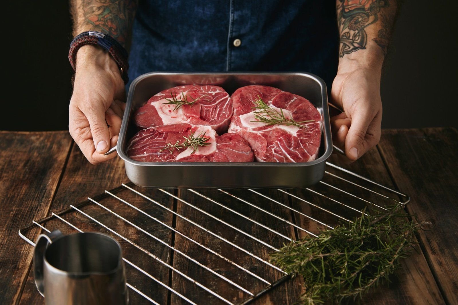 Hands holding a steel tray with three thick bone-in raw beef steaks.